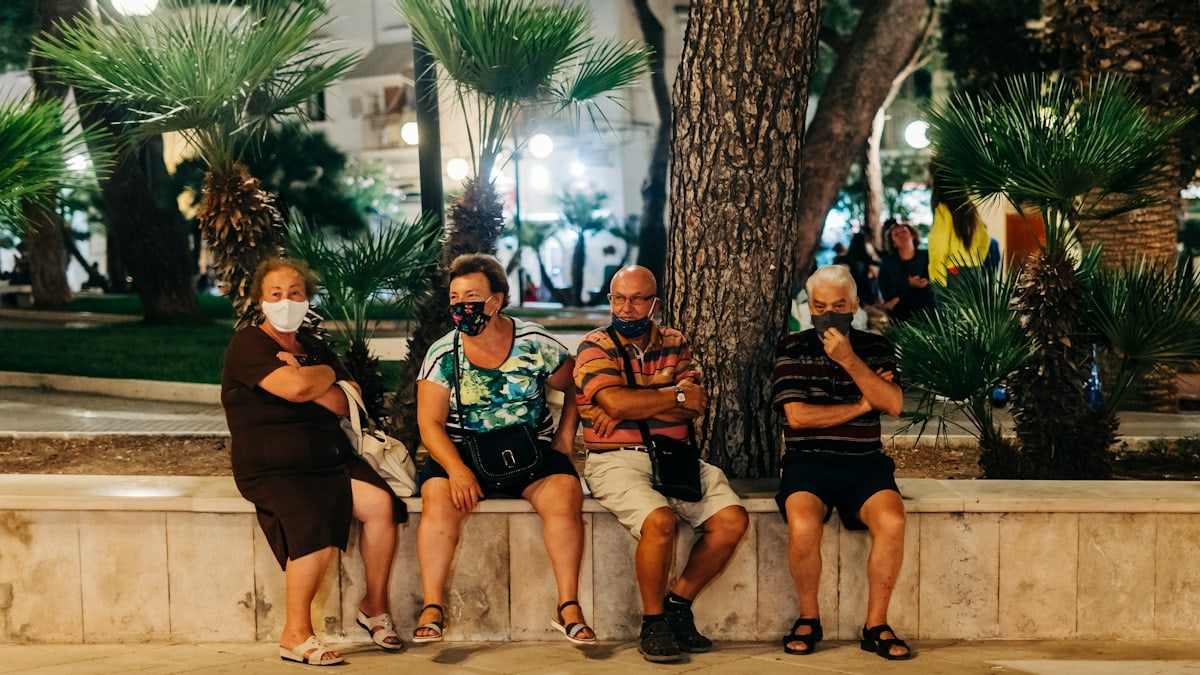 Two elderly couples wearing face masks sit people watching in a square in Puglia, Italy